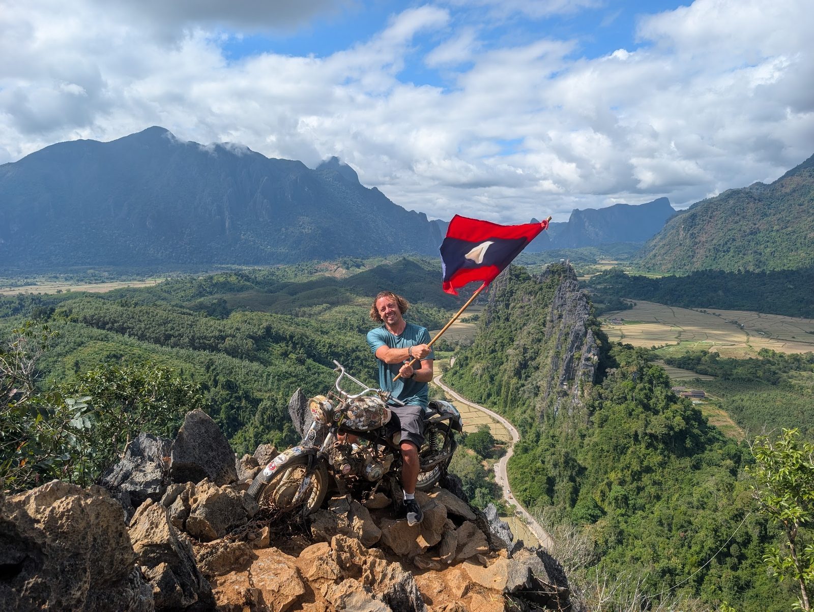 Ken waving the Laos flag on a mountaintop